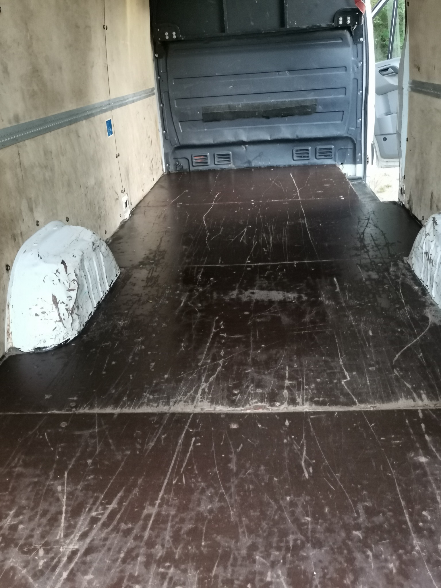 Wnętrze pustej przestrzeni ładunkowej busa z drewnianą podłogą i ścianami, widoczne ślady użytkowania i mocowania na ścianach.