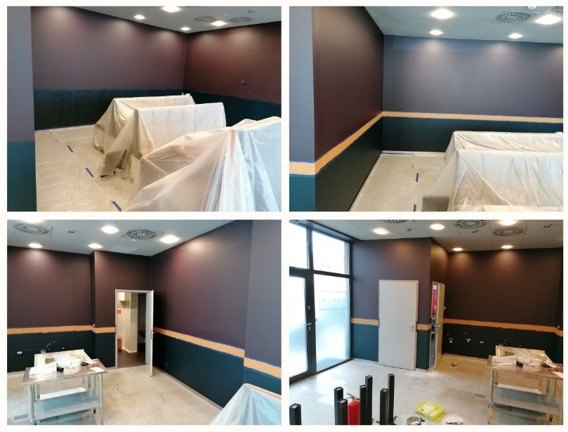 Wnętrze biurowe w trakcie malowania: ściany w dwóch odcieniach fioletu i granatu, zabezpieczone meble pod folią, widoczne taśmy malarskie i metalowy stolik z narzędziami malarskimi.