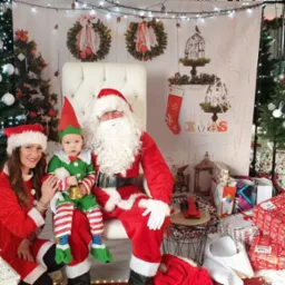 Sesja zdjęciowa z Mikołajem i elfem na tle świątecznej scenografii z choinkami i prezentami.