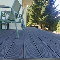 Paweł Walburg USŁUGI STOLARSKIE - Nowoczesny taras z desek kompozytowych w odcieniach szarości, z zielonymi krzesłami ogrodowymi i widokiem na iglaste drzewa w tle.