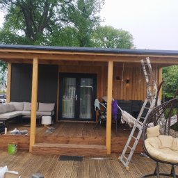 Paweł Walburg USŁUGI STOLARSKIE - Zadaszony taras drewniany w trakcie wykańczania, widoczna drabina, farba, meble ogrodowe i huśtawka wisząca