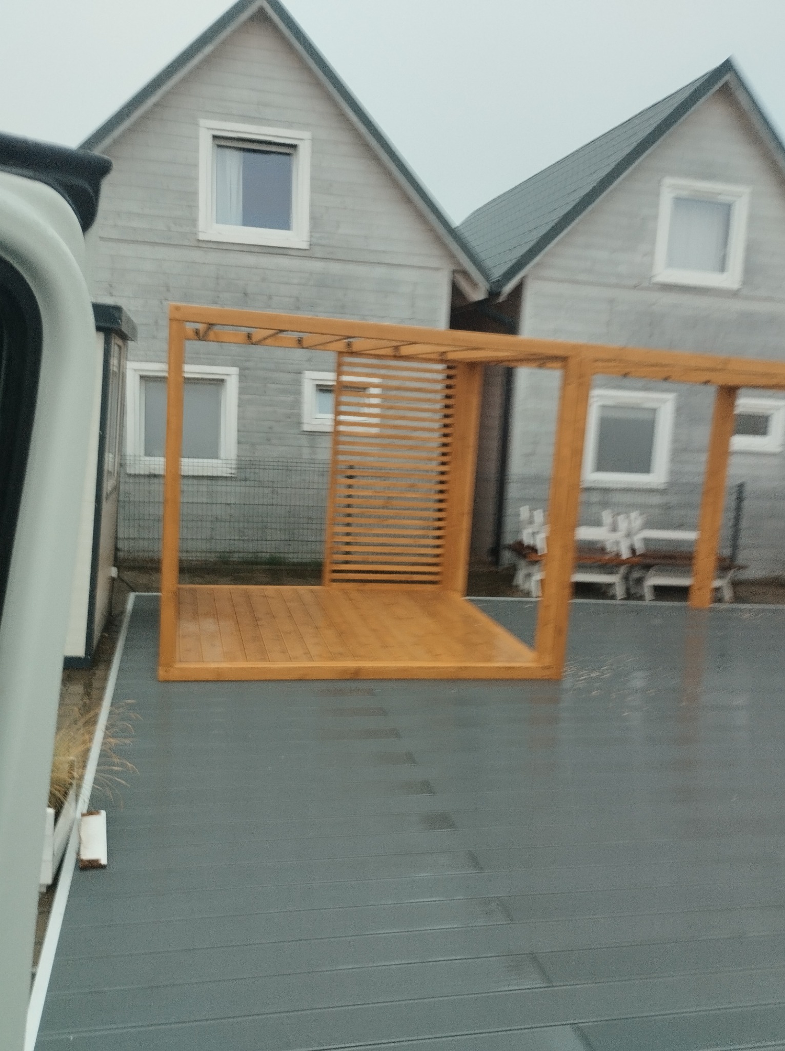 Surowa drewniana konstrukcja z lamelami, przypominająca szkielet przyszłej pergoli, widoczna na tle szarych domów w Trzebiatowie. Konstrukcja stoi na szarym podłożu, prawdopodobnie tarasie.