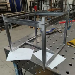 Metalowa konstrukcja szkieletowa, prawdopodobnie stelaż meblowy, spawana w Koleczkowie, ustawiona na perforowanym stole warsztatowym z widocznymi narzędziami i rysunkiem technicznym.