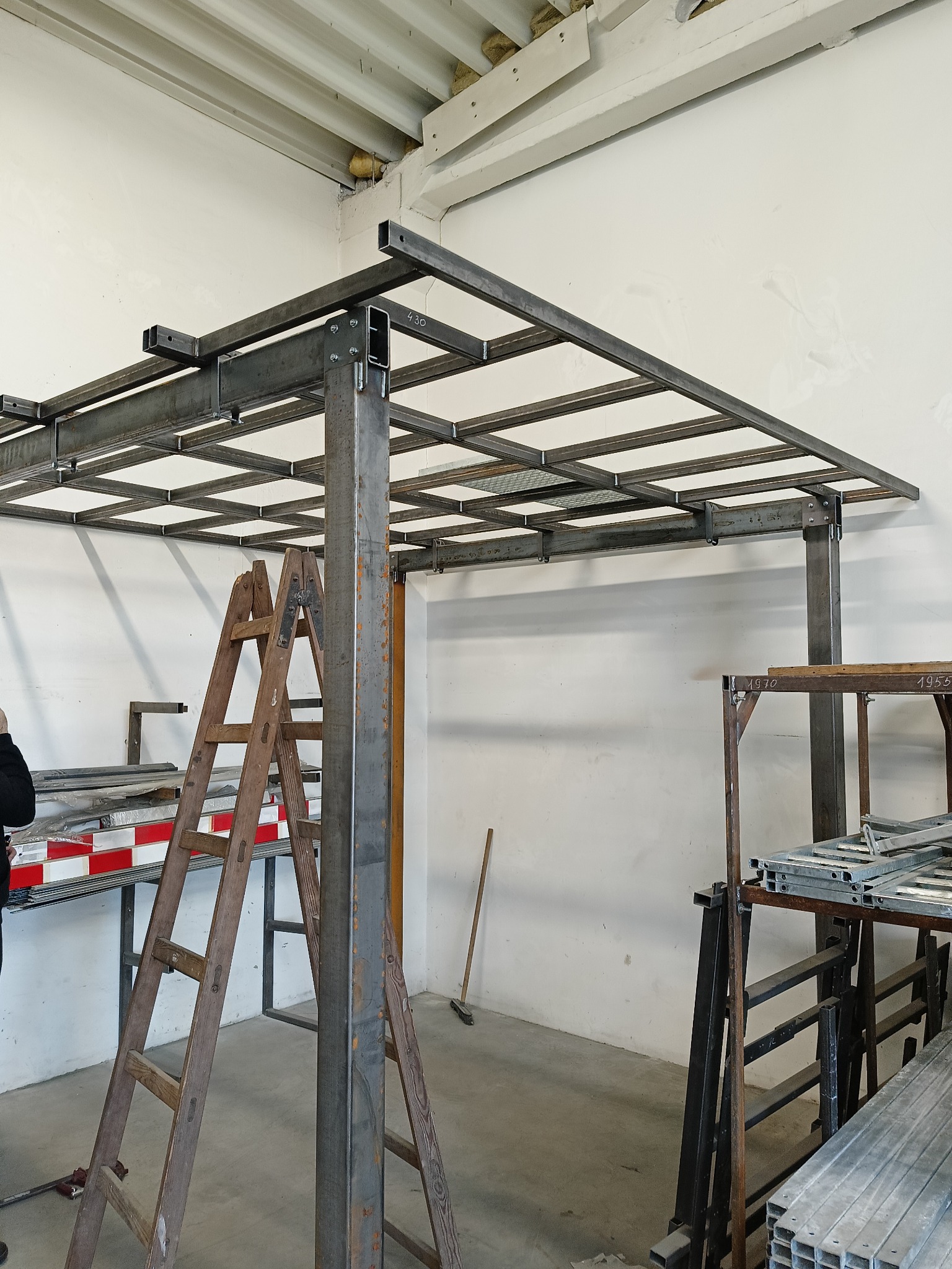 Wewnętrzna konstrukcja stalowa hali w trakcie budowy, widoczna drewniana drabina oparta o pionowy słup, w tle biała ściana i elementy konstrukcji dachu