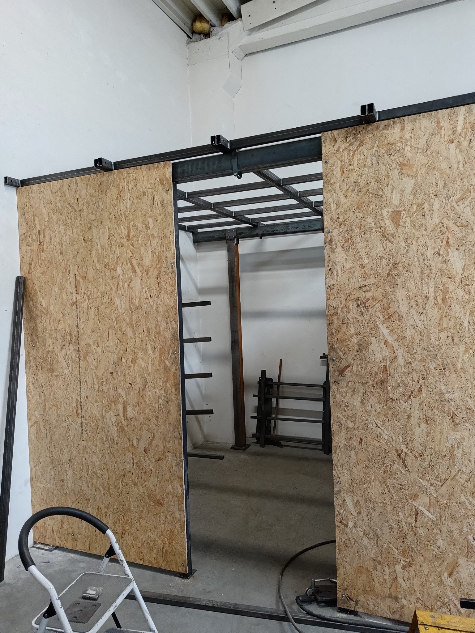 Konstrukcja stalowa z przesuwnymi drzwiami z płyty OSB w hali, widoczna drabina i elementy konstrukcji stropu.