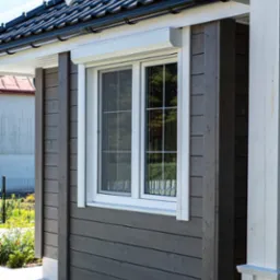 Białe okno z roletą zewnętrzną w kasecie na drewnianej elewacji domu z widoczną konstrukcją wspornikową dachu.