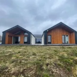 Nowoczesny dom modułowy z drewnianą elewacją i dużymi oknami, widok z niskiej perspektywy na tle pochmurnego nieba.