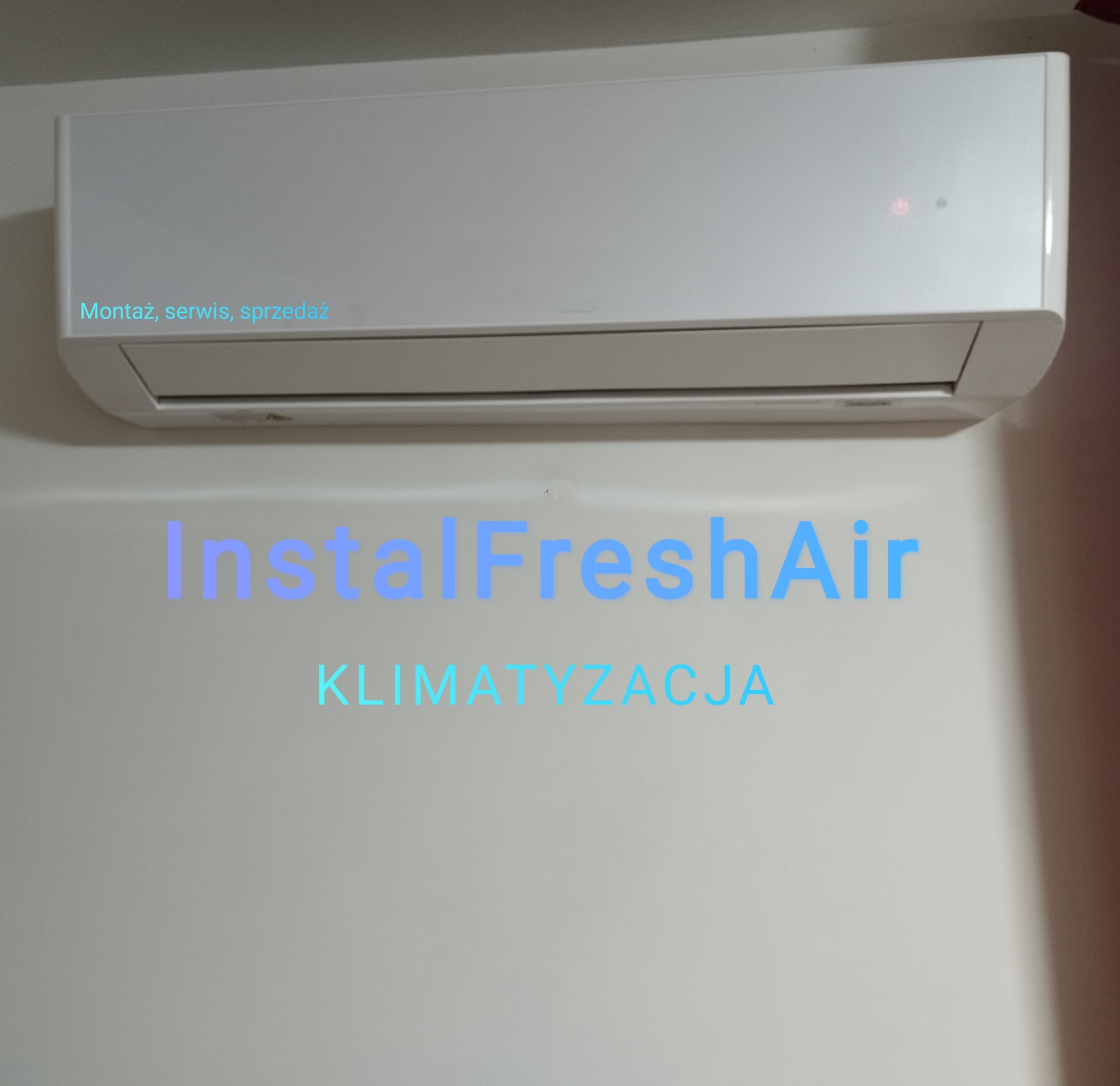 Biała jednostka klimatyzacji ściennej z czerwoną diodą, zamontowana na jasnej ścianie z napisem 'InstalFreshAir KLIMATYZACJA'.