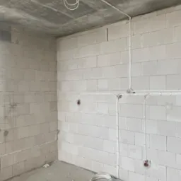 Surowy stan wnętrza z widoczną instalacją elektryczną: przewody prowadzone po ścianach z betonu komórkowego, gniazda w puszkach, pętle kabli zwisające z sufitu i leżące na podłodze.