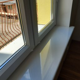 Agnieszka Kwiatkowska - Błyszczący parapet z PCV po umyciu, widok z góry na okno z widoczną, zewnętrzną, żółtą ścianą budynku i balkonem z metalową balustradą.