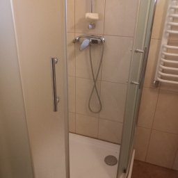 Agnieszka Kwiatkowska - Kabina prysznicowa z chromowaną armaturą na tle beżowych płytek, widoczny odpływ i grzejnik drabinkowy.