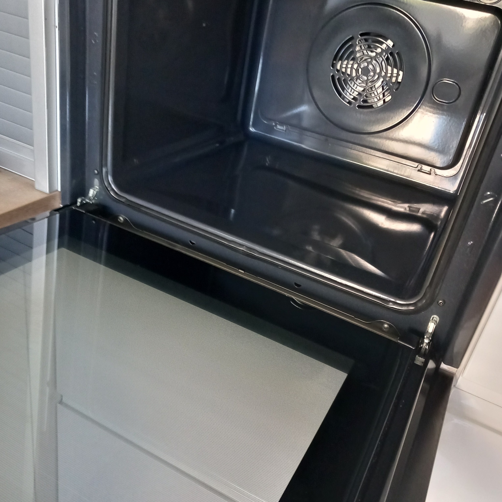 Wnętrze czystego piekarnika elektrycznego z widocznym wentylatorem i lekko uchylonymi drzwiczkami z szybą.