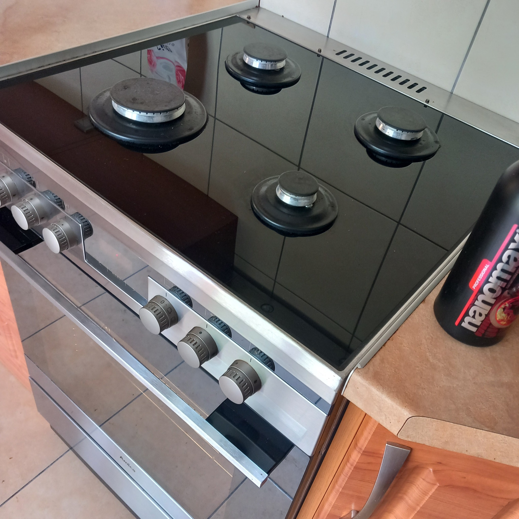 Czteropalnikowa płyta indukcyjna z widocznymi zabrudzeniami na szklanej powierzchni i palnikach, obok stoi czarna butelka środka czyszczącego Nanomax Professional.