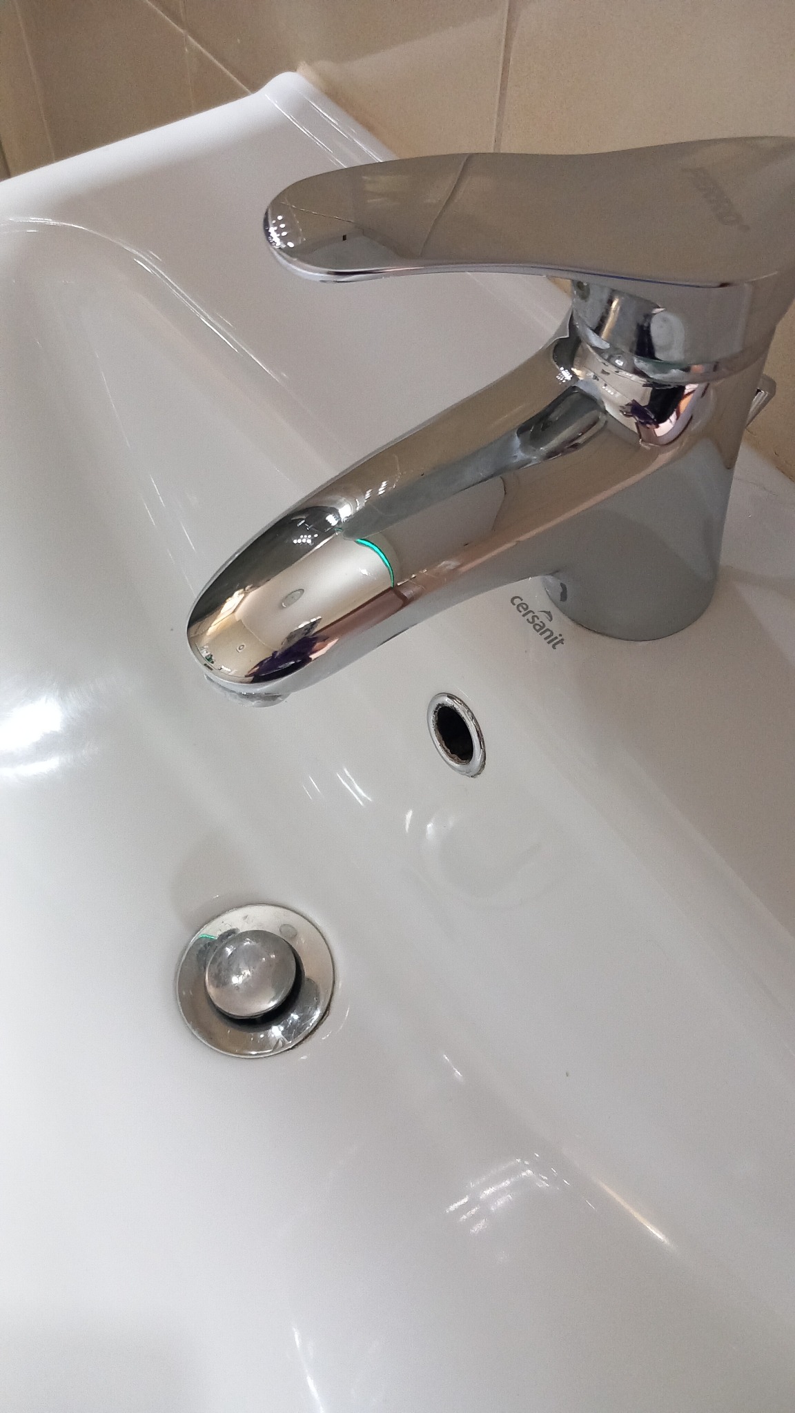 Biała umywalka Cersanit z chromowaną baterią, widoczny odpływ i odbicie światła na powierzchni.