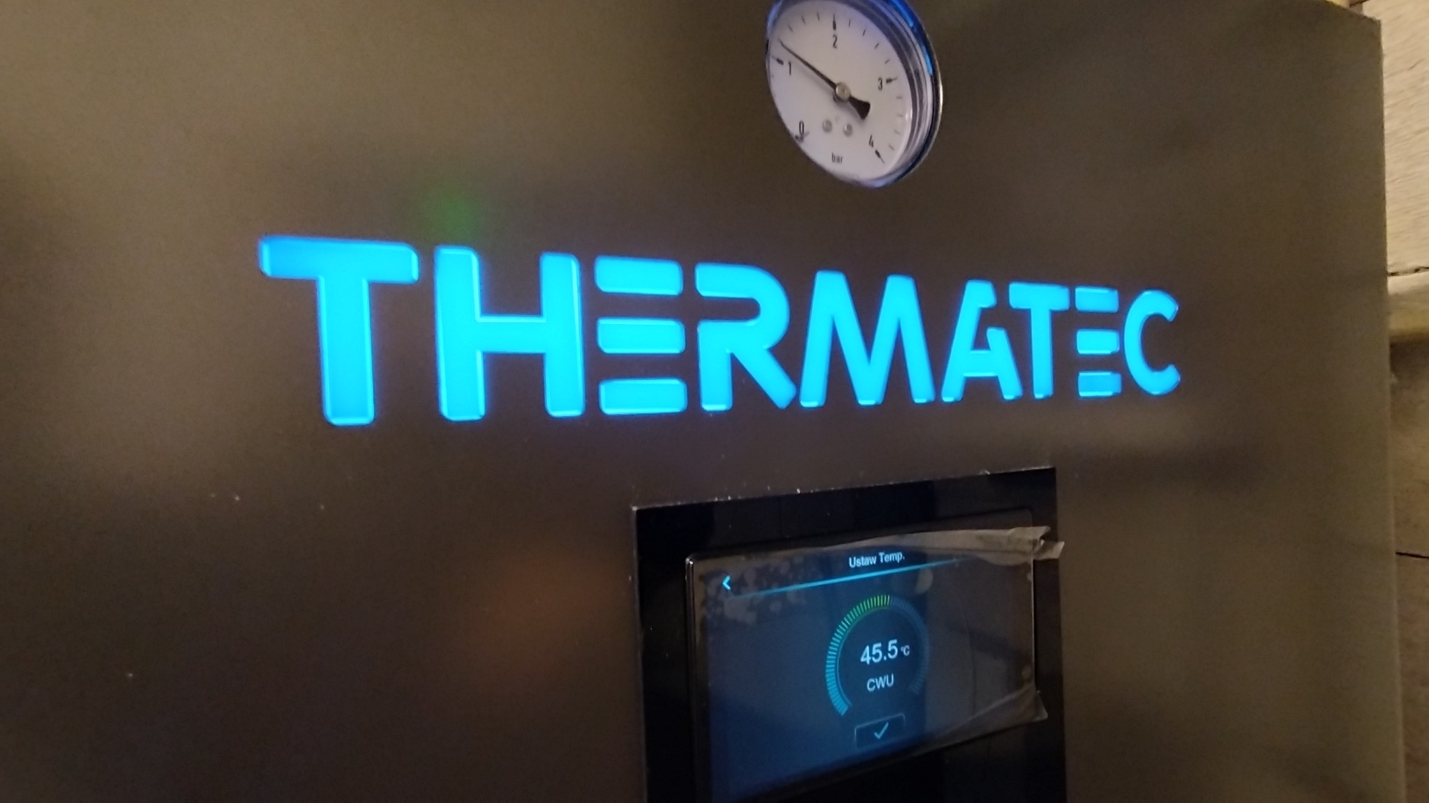 Szczegółowe ujęcie panelu sterowania urządzenia THERMATEC z wyświetlaczem ustawionej temperatury CWU na 45.5 stopni Celsjusza oraz analogowym manometrem ciśnienia.