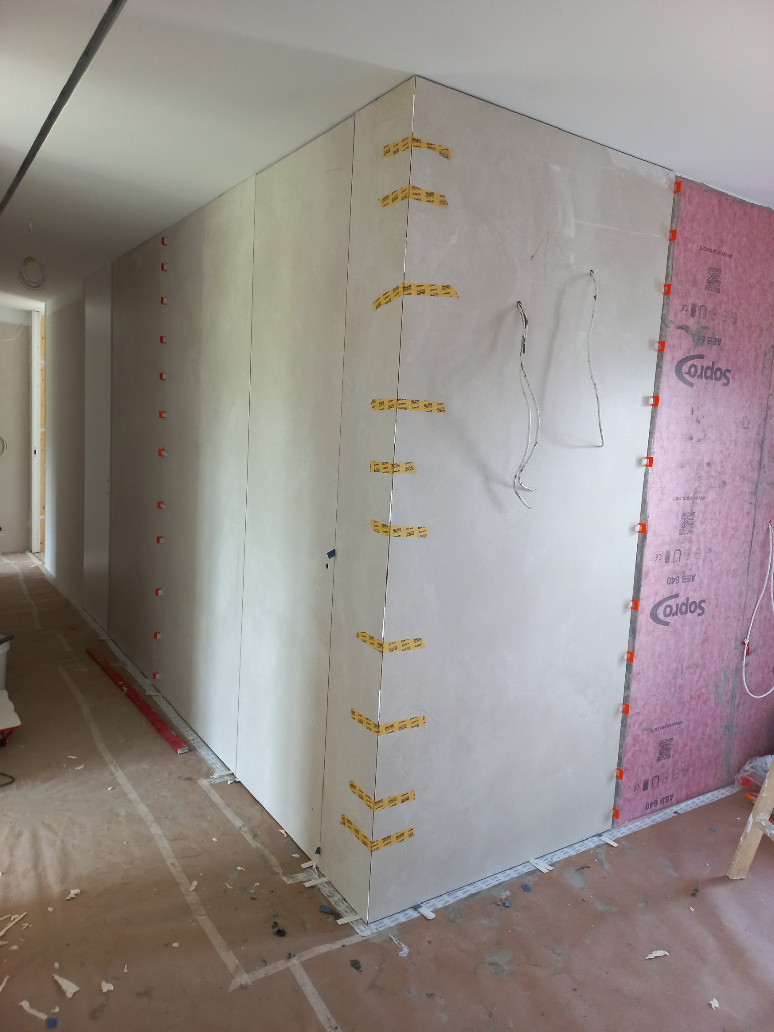 Ściany w trakcie montażu płyt gipsowo-kartonowych, narożniki zabezpieczone taśmą, widoczne przewody, płyta Soprod AEB 640, podłoga zabezpieczona folią malarską.