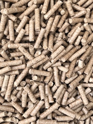 Stos cylindrycznych brykietów z biomasy drzewnej o naturalnym odcieniu beżu, ułożonych chaotycznie na płaskiej powierzchni, widoczne delikatne ślady obróbki drewna.