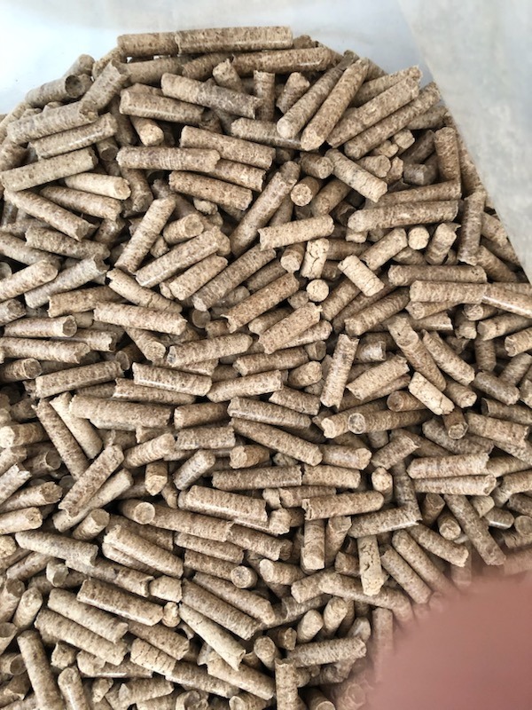 Jasne, cylindryczne brykiety z biomasy, prawdopodobnie z trocin drzewnych, wypełniające przezroczysty worek, widok z góry.