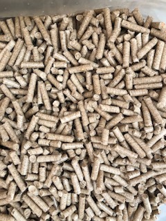 Jasne, cylindryczne granulki biomasy drzewnej wypełniające kadr, widoczne drobne wióry i nierówności na powierzchni pelletu, oświetlenie dzienne.