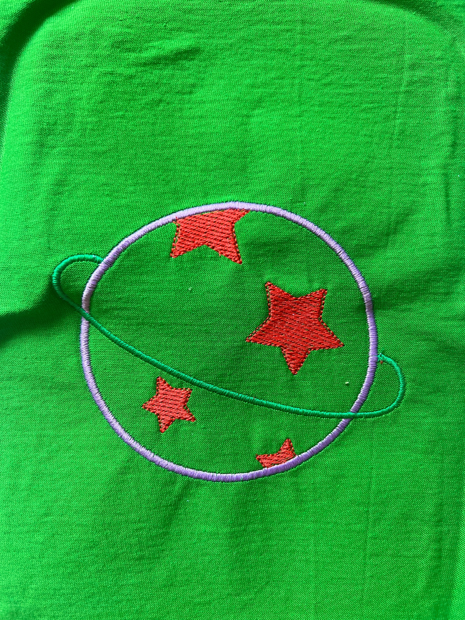 Jasnozielona tkanina z wyhaftowanym motywem planety z czerwonymi gwiazdami wewnątrz, obwiedzionej fioletową linią i zielonym pierścieniem.