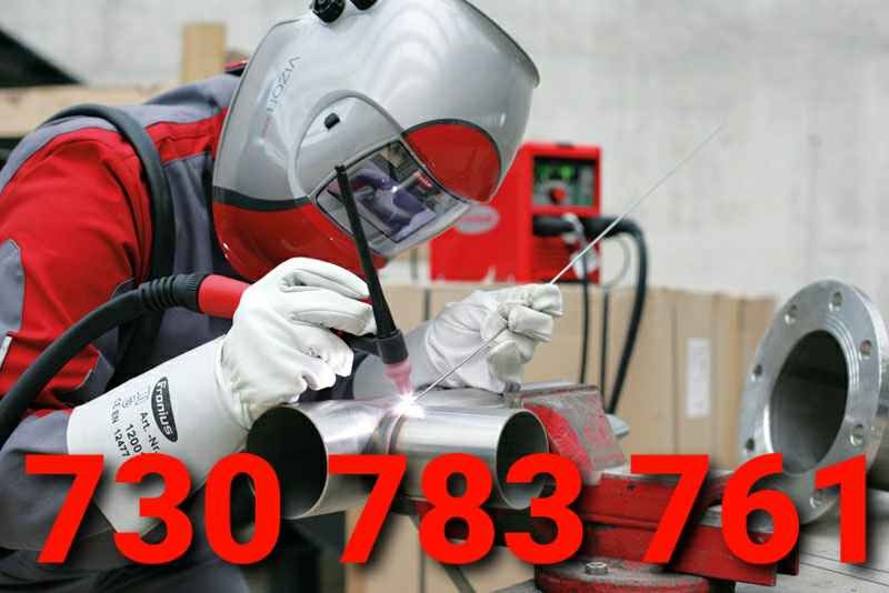 Pracownik w masce spawalniczej łączy dwa metalowe rury w Jonkowie, używając spawarki TIG. Na pierwszym planie widoczny uchwyt spawalniczy i błysk spawania, w tle czerwona spawarka i metalowy kołnierz.