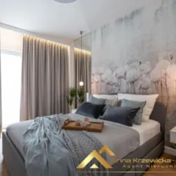 Nowoczesna sypialnia z łóżkiem, narzutą w warkoczowy wzór, drewnianą tacą z filiżankami, krzesłem na złotych nogach i tapetą w motyw flamingów.