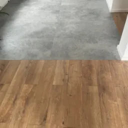 Połączenie szarych płytek podłogowych w kuchni z drewnopodobnymi panelami w salonie, widoczne nierówne wykończenie przy ścianie.