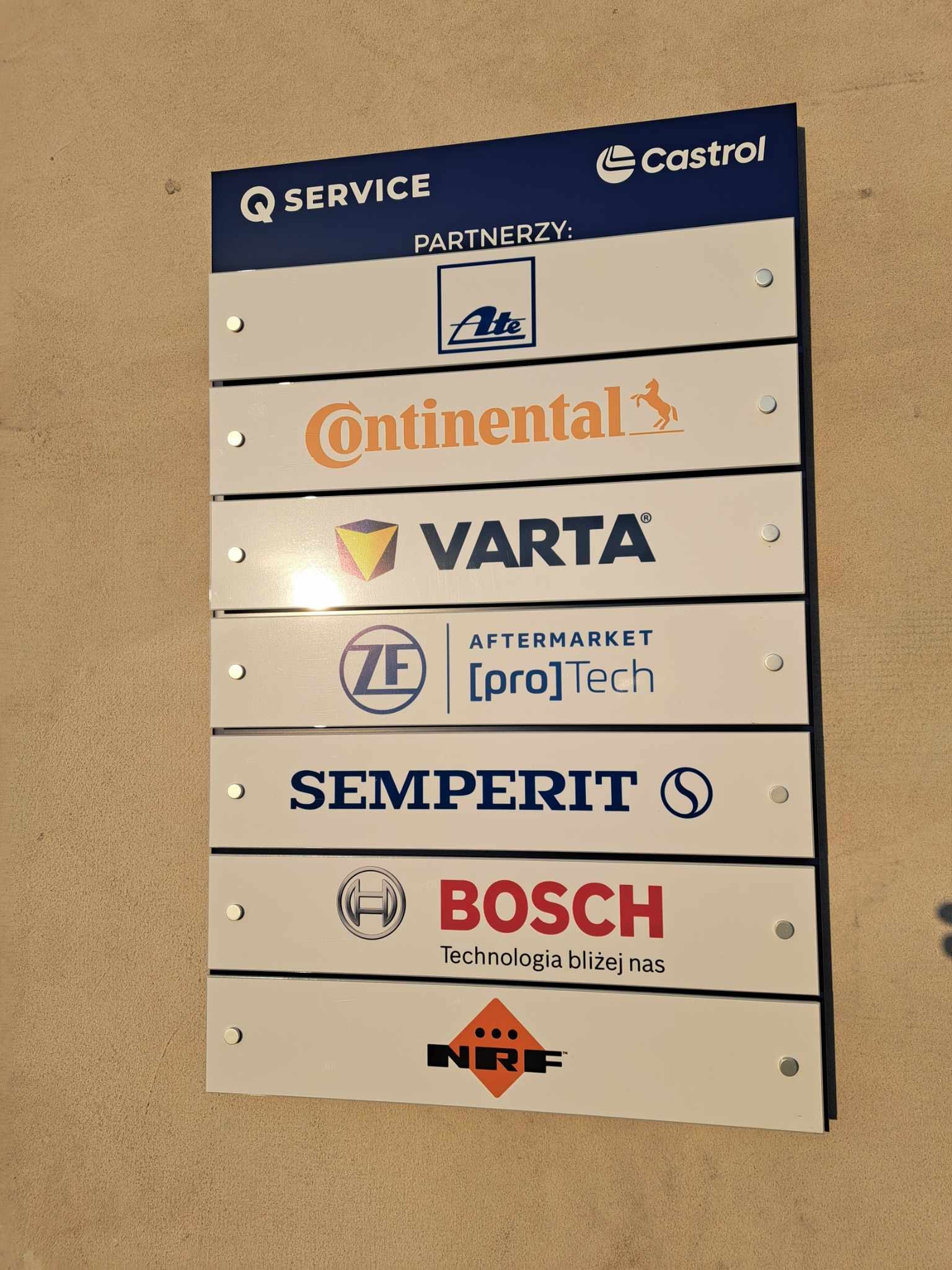 Tablica informacyjna z logotypami partnerów serwisu samochodowego, w tym Castrol, Ate, Continental, Varta, ZF [pro]Tech, Semperit, Bosch i NRF.