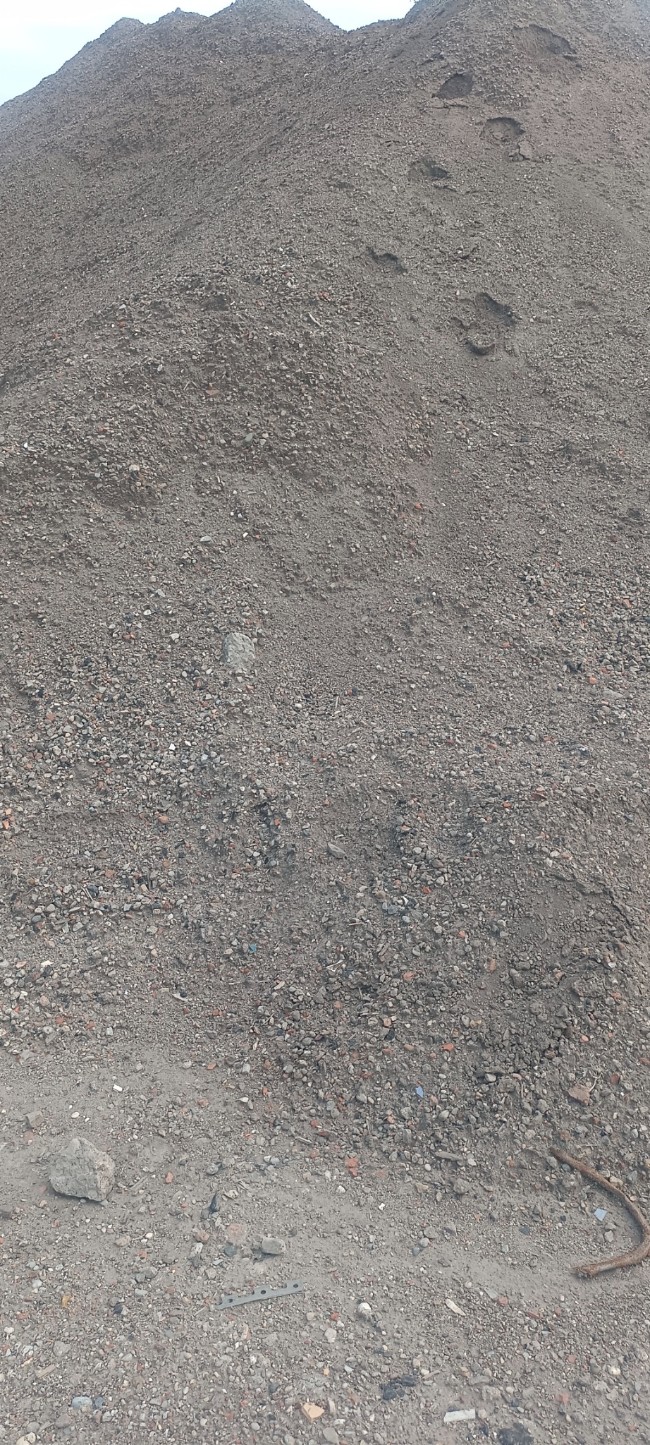 Góra piasku i żwiru z widocznymi odciskami butów na zboczu, w dolnej części fragment zardzewiałego pręta.