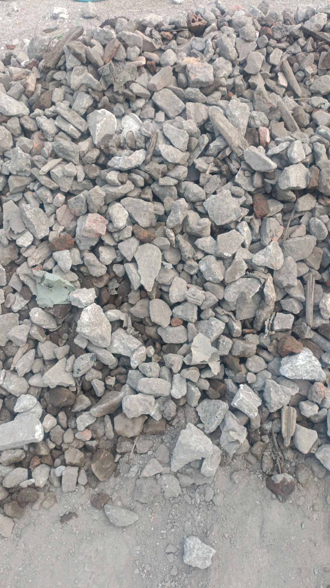 Stos gruzu i resztek budowlanych, głównie szarego betonu i cegieł, na szarej, piaszczystej powierzchni.