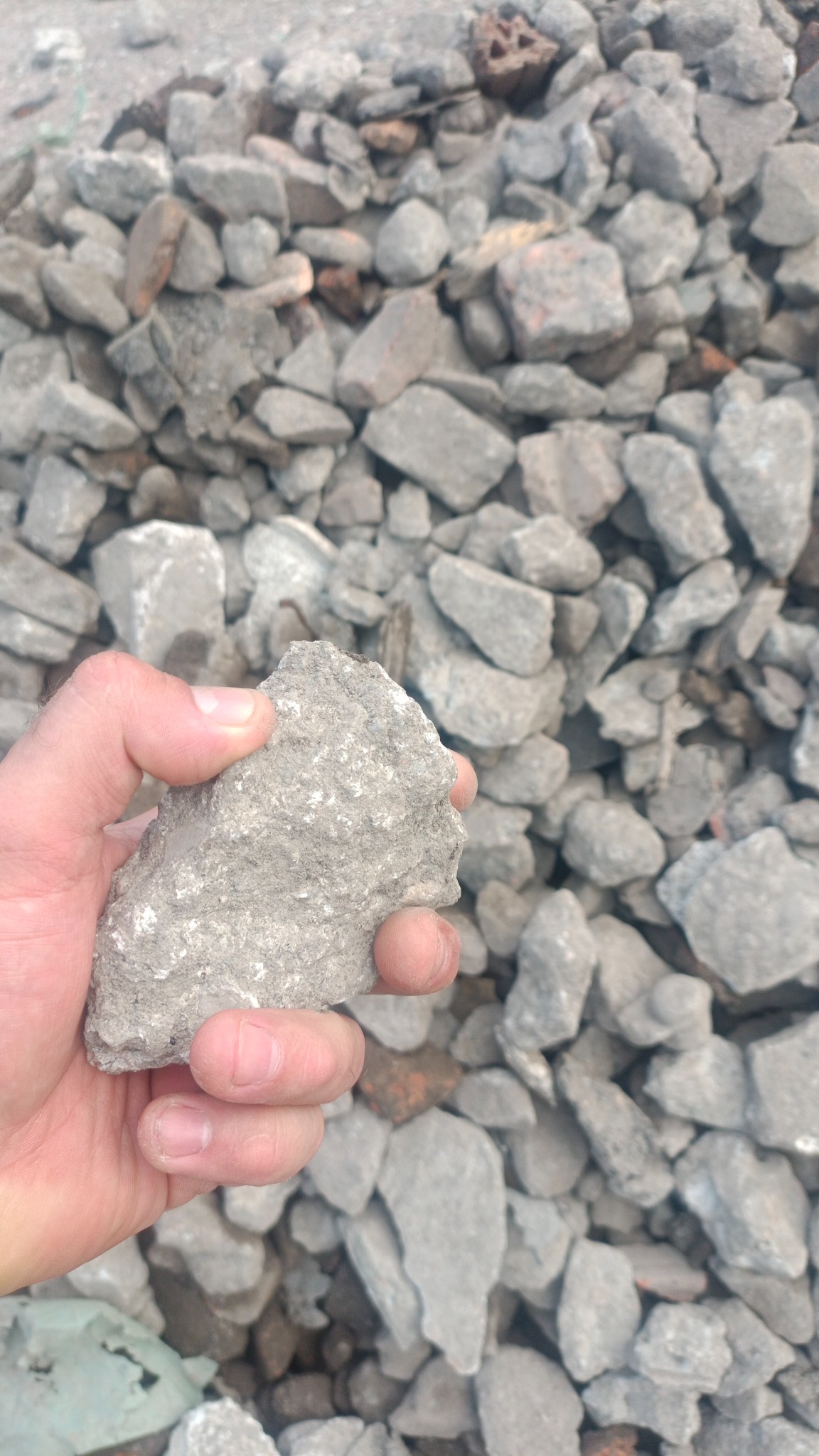 Dłoń trzymająca kawałek gruzu na tle sterty gruzu z cegieł i betonu.