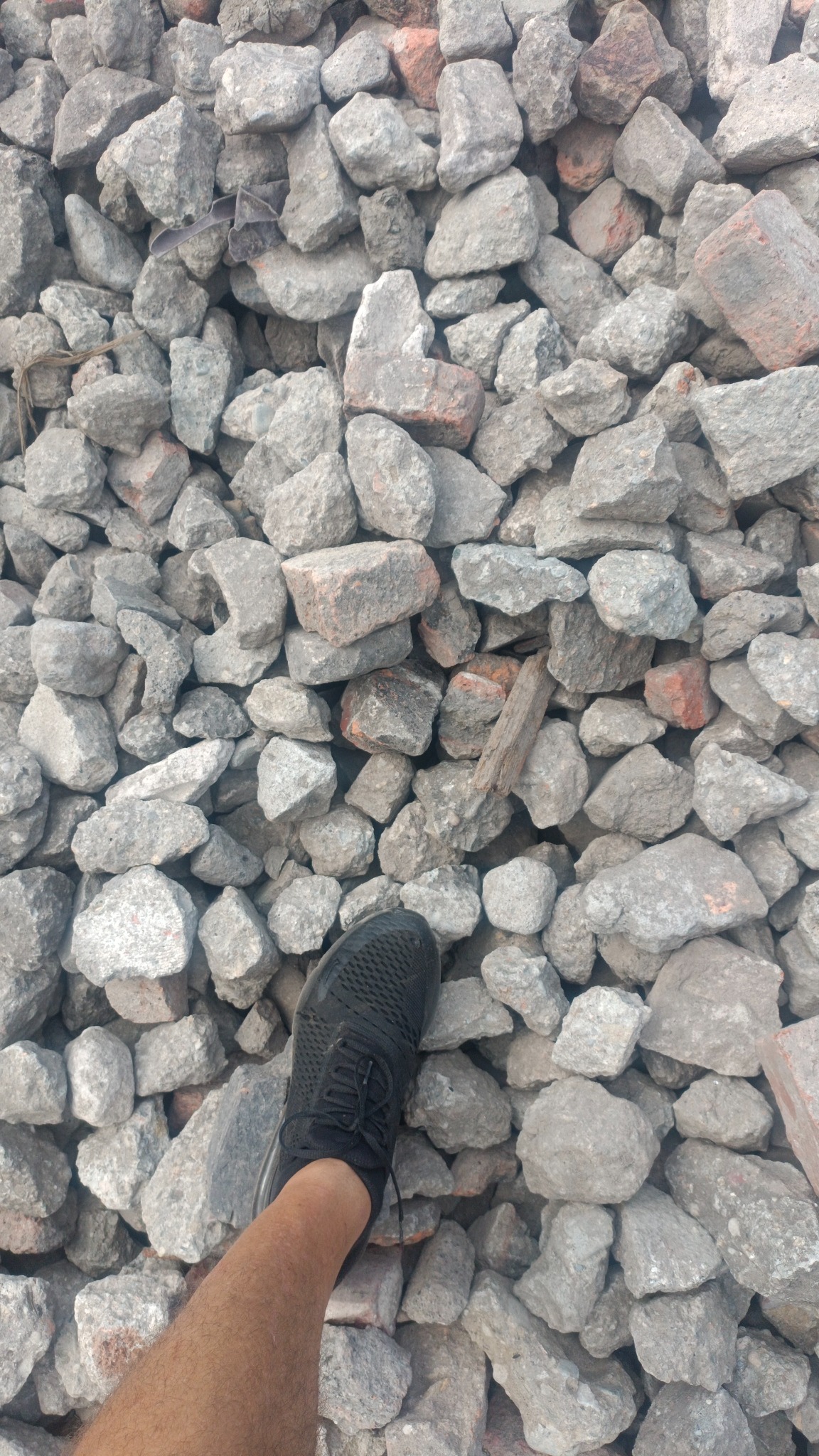 Stopa w czarnym sportowym bucie stoi na gruzowisku z kamieni i fragmentów cegieł.
