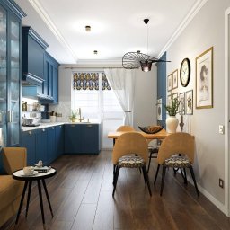 Komarova Design - Niebieska kuchnia z jadalnią: eleganckie szafki z przeszklonymi witrynami, marmurowy blat, drewniany stół z beżowymi krzesłami w geometryczne wzory, dekoracyjne zasłony i lampa w stylu retro.