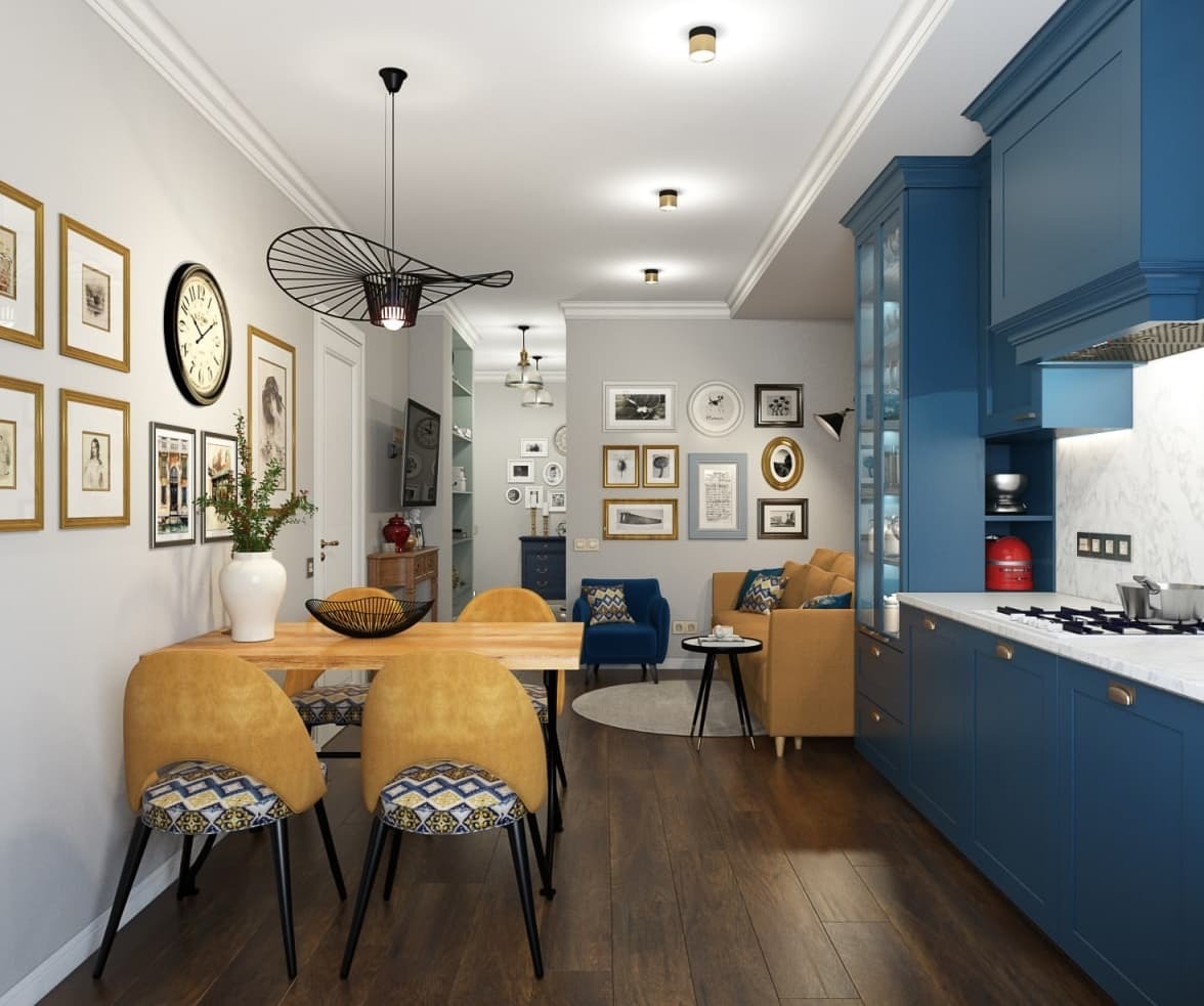 Wnętrze mieszkania z otwartą kuchnią i jadalnią, niebieska zabudowa kuchenna, drewniany stół z żółtymi krzesłami, galeria obrazków na ścianie, widok na salon.
