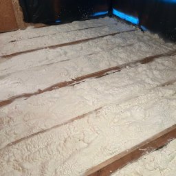 THERMONOVA Dorota Dziemidowicz - Poddasze po ociepleniu pianką PUR, widoczne drewniane belki i warstwa izolacji. Czarna folia w rogu pomieszczenia.