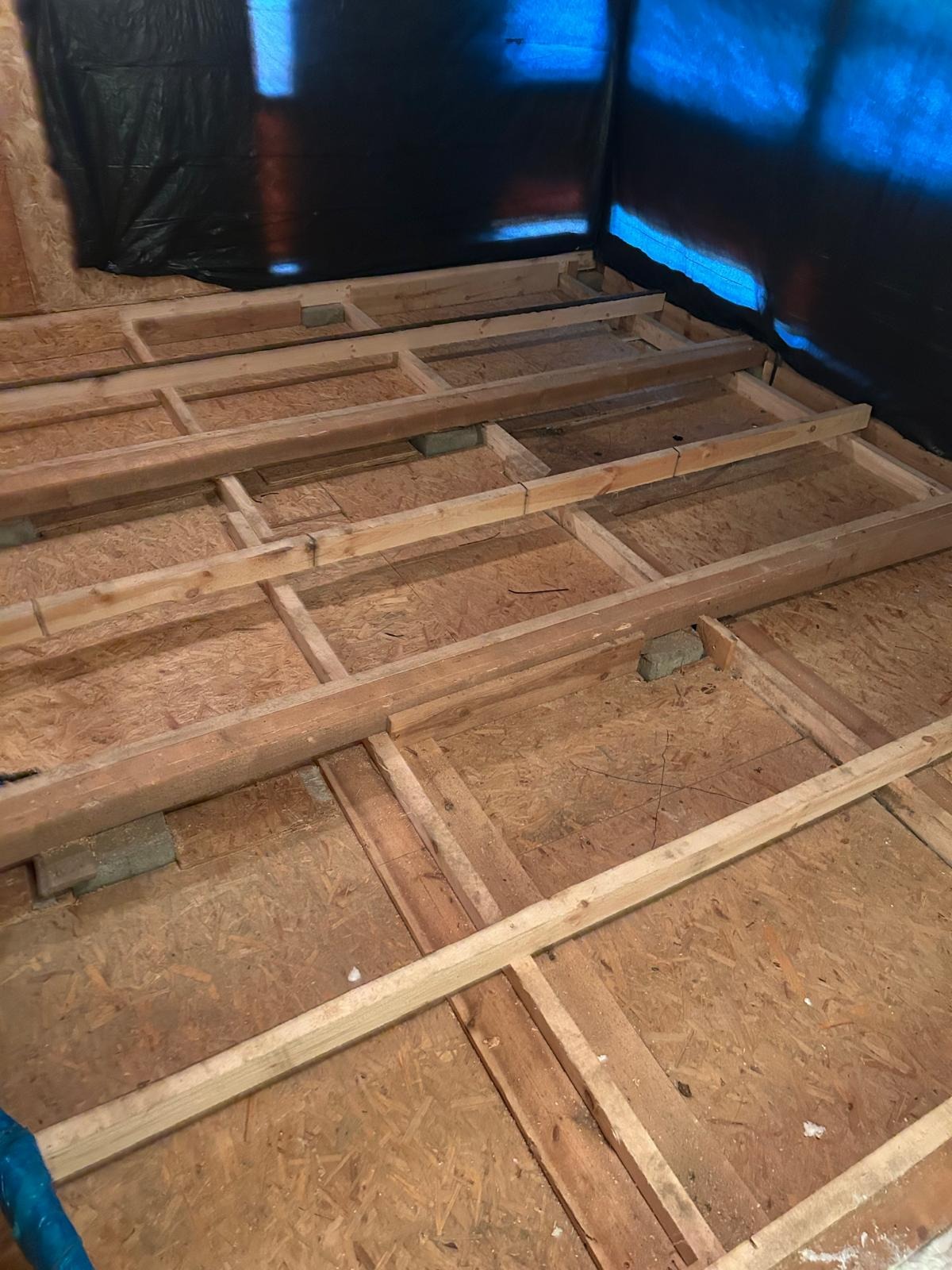 Drewniana konstrukcja pod podłogę na poddaszu, przygotowana do ocieplenia, z widoczną folią ochronną na ścianach. Detal: cegły podtrzymujące konstrukcję.