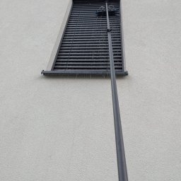 LTD Agnieszka Opioła C&M Clean and more - Mycie żaluzji zewnętrznych na elewacji budynku przy użyciu teleskopowej lancy z szczotkami. Woda spływa po lamelach.