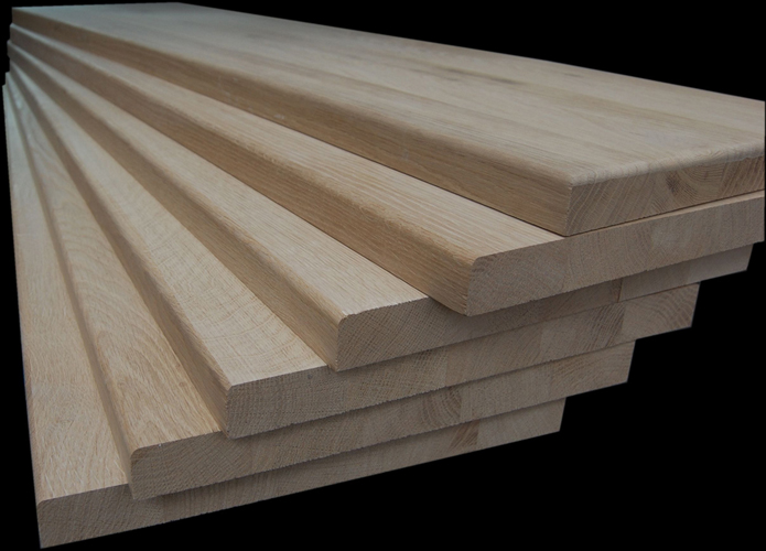 Stos surowych, dębowych stopni schodowych z zaokrąglonymi krawędziami, przygotowanych do montażu, na czarnym tle.