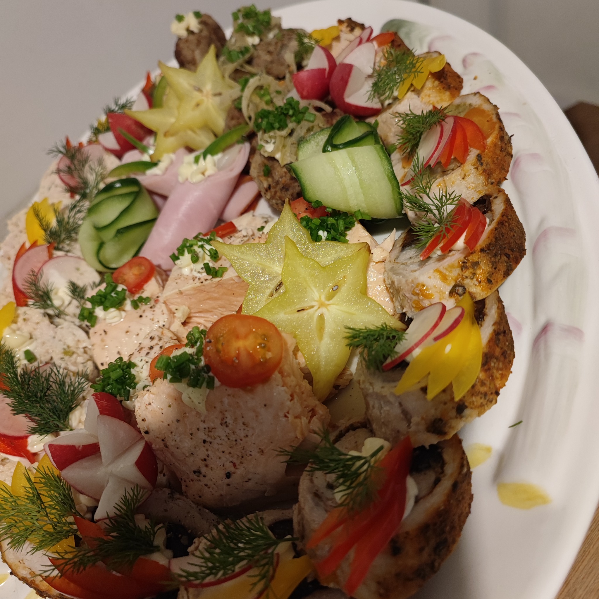 Dekoracyjna taca z roladkami mięsnymi, wędlinami, kulkami mięsnymi, plastrami ogórka, rzodkiewkami i karambolą, udekorowana koperkiem i sosem majonezowym.