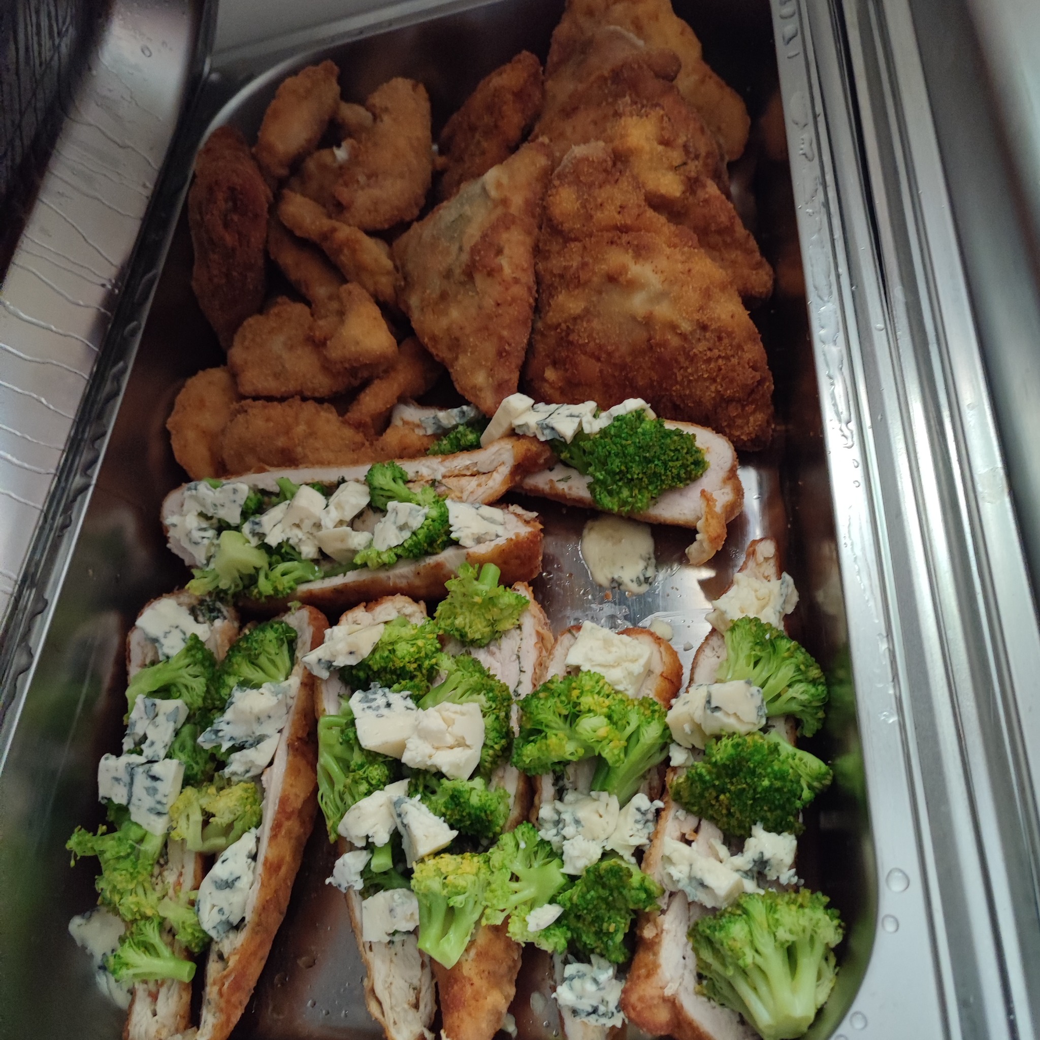 Metalowa taca z porcją smażonych kotletów i plastrów mięsa drobiowego z brokułami i serem pleśniowym.