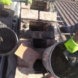 Prace murarskie na dachu: wznoszenie komina z cegły, widoczne zaprawa, cegły, drabina dachowa i dłonie w roboczych rękawicach. Częściowo zrekonstruowany komin z otworami.