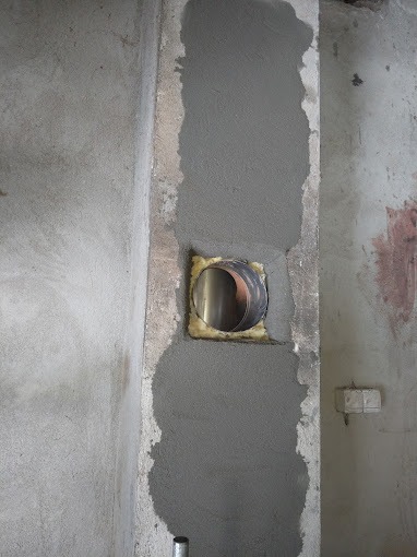 Montaż przewodu wentylacyjnego w ścianie, widoczne świeże obłożenie zaprawą wokół otworu, fragment instalacji elektrycznej w tle.