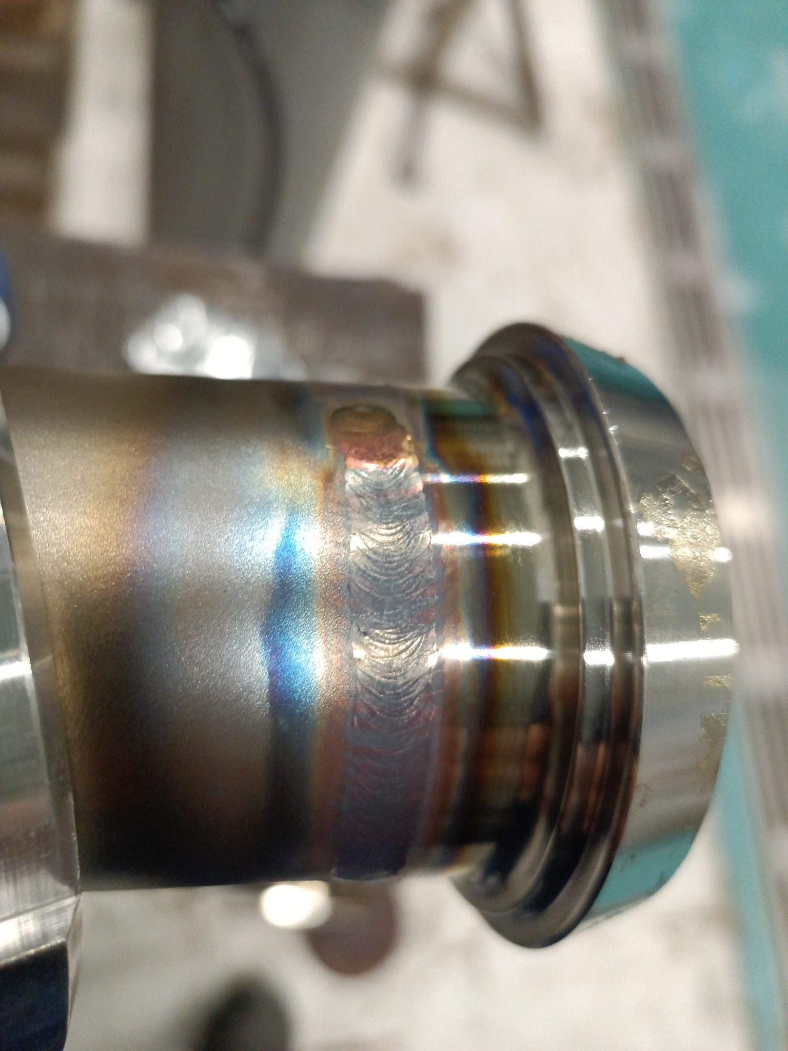 Detaliczne zbliżenie na spawany element metalowy z widocznymi śladami spawania i opalizującymi przebarwieniami termicznymi.