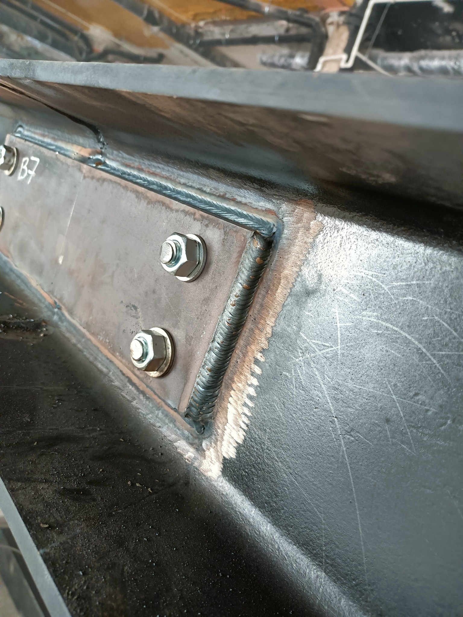 Spoina łącząca dwie metalowe belki, wzmocniona dodatkową płytką przykręconą śrubami z nakrętkami, widoczne ślady szlifowania i numer B7.