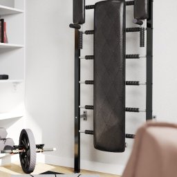 Pracownia Architektury Wnętrz Klaudia Woźniak - Ścianka gimnastyczna z czarną tapicerowaną ławką, drabinkami i drążkami, obok mata do ćwiczeń z napisem 'Easy Yoga' oraz sprzęt do ćwiczeń z obciążeniami, na tle białej ściany i regału.