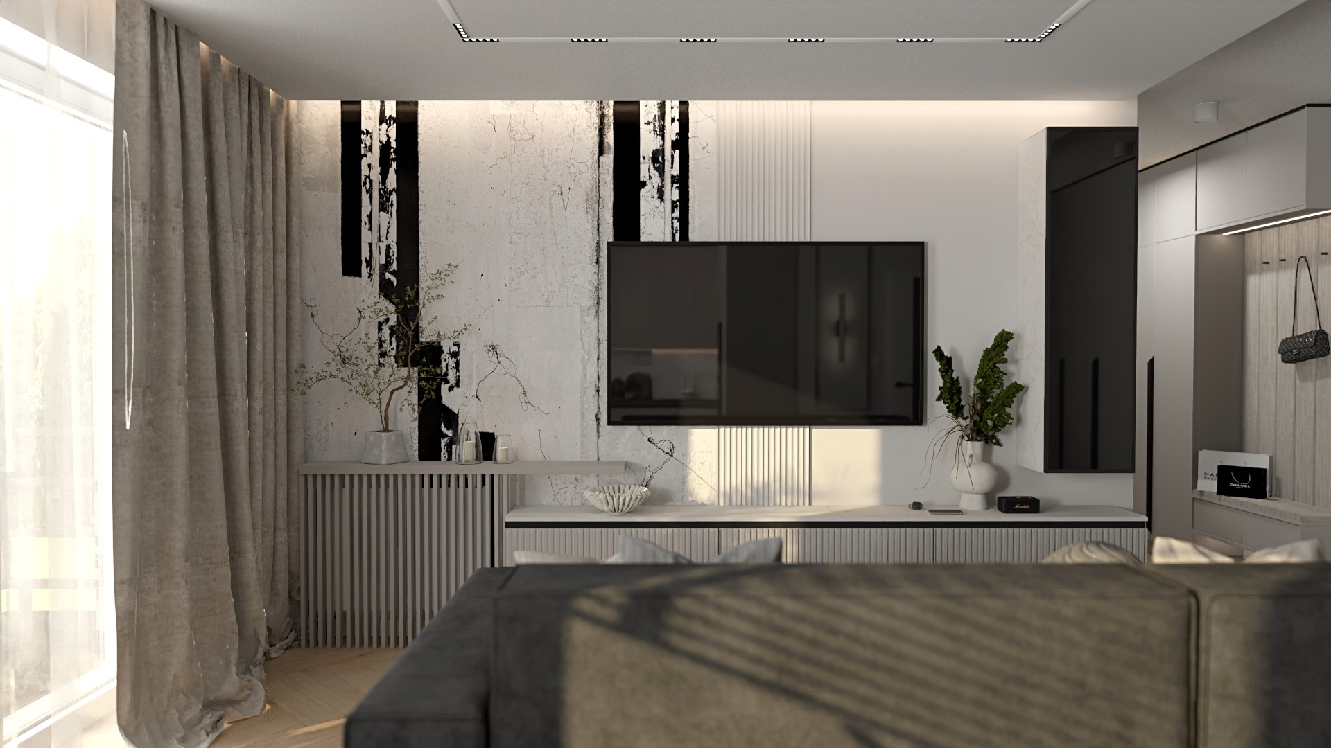 Nowoczesny salon z telewizorem, dekoracyjną ścianą z czarnymi akcentami, roślinami w wazonach i szarym narożnikiem z widoczną teksturą materiału.