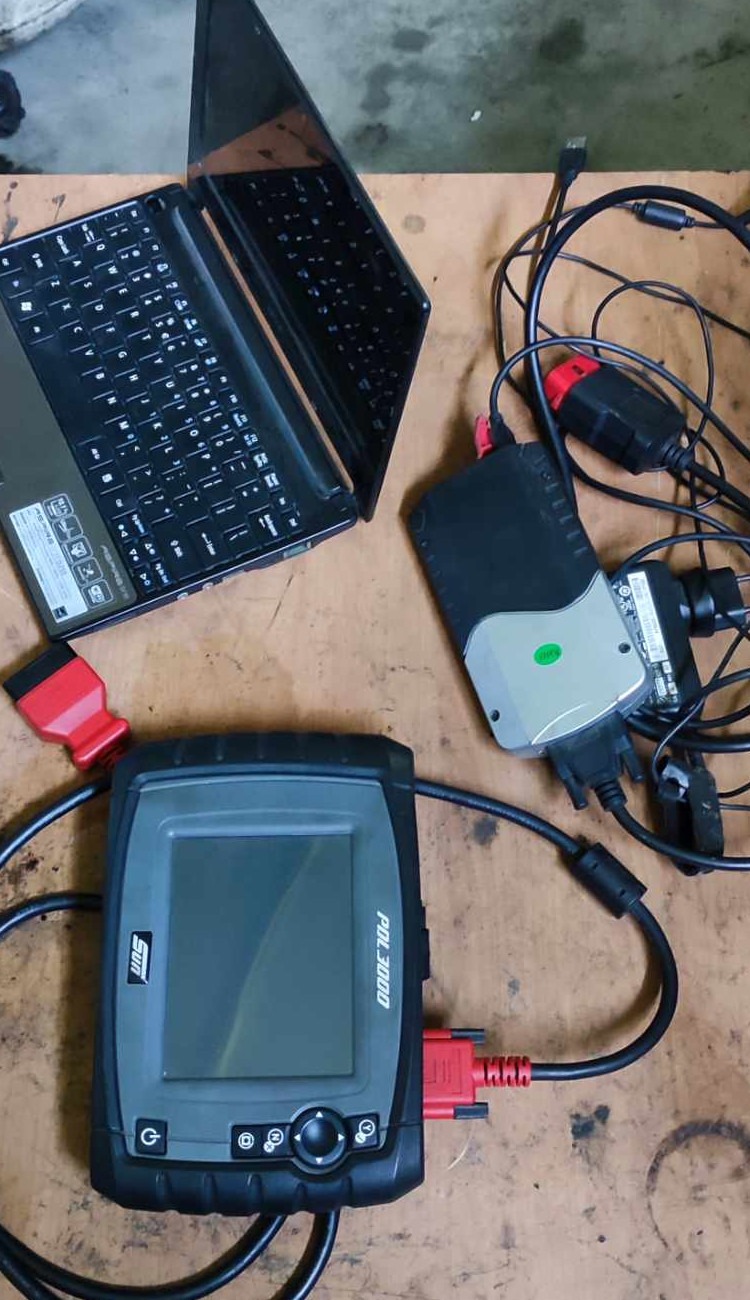 Laptop, interfejs diagnostyczny i skaner OBD podłączone kablami na roboczym stole, przygotowane do diagnostyki samochodowej.