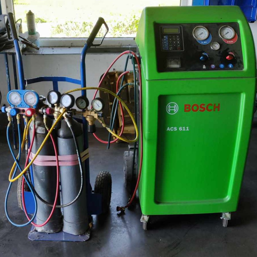 Zielone urządzenie Bosch ACS 611 do obsługi układów klimatyzacji samochodowej, z podłączonym wózkiem z butlami i manometrami, widoczne przewody i złączki.