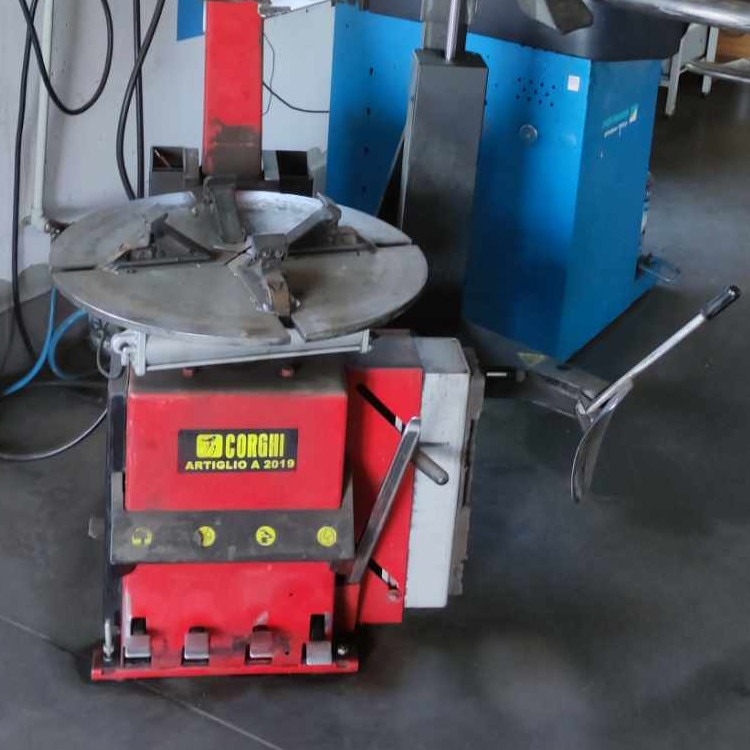 Czerwono-szara montażownica do opon marki Corghi Artiglio A 2019 na tle niebieskiej wyważarki w warsztacie.