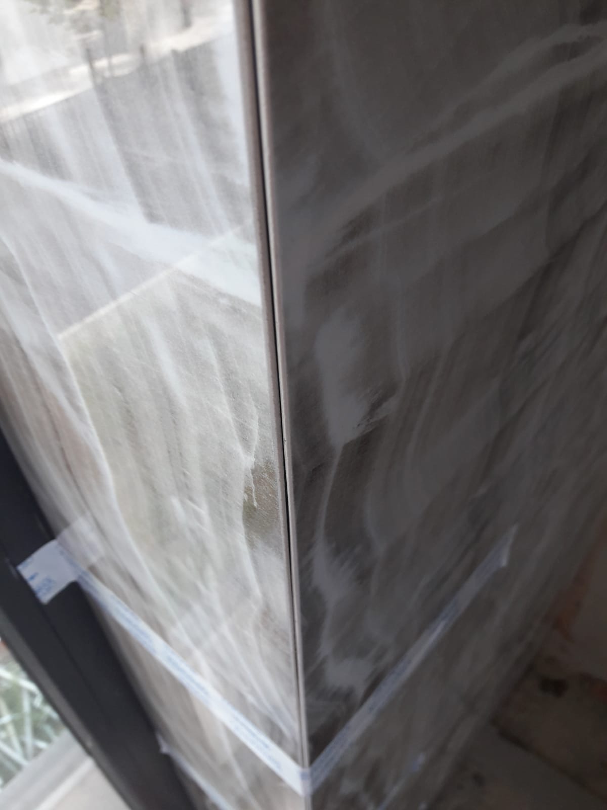 Połączenie dwóch ścian wyłożonych płytkami imitującymi marmur, zabezpieczonych taśmą malarską na czas schnięcia kleju.